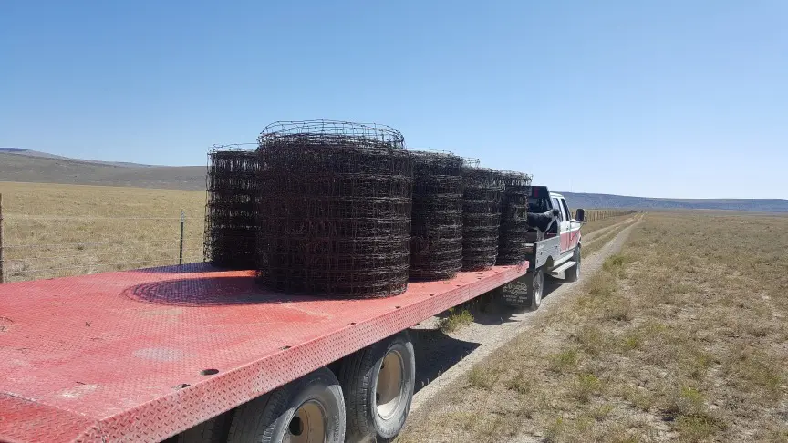 Truck carrying fencing rolls in open landscape.