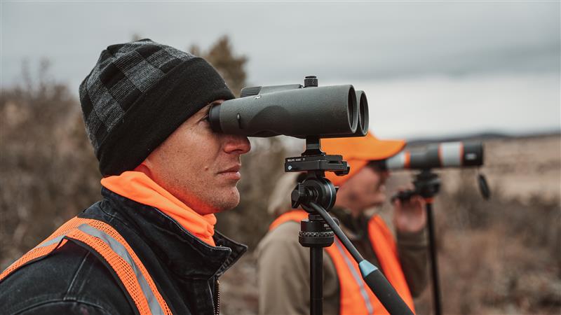 Hunters observing wildlife with binoculars in a natural setting.